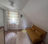 Living space in a cottage with a yellow sofa and wood-patterned flooring.