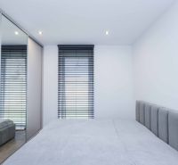 A bedroom in a family house with a bed, a mirrored wardrobe, and blinds on the window.