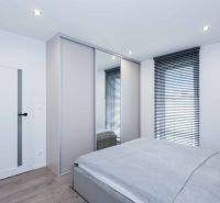 A bedroom in a family house with a bed, a wardrobe, and a wooden decor floor.