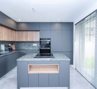 A kitchen in a family house with modern cabinets and large windows with blinds.
