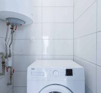 A washing machine and a boiler in the bathroom of a family house with white tiles.