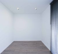 An empty room with wood-patterned flooring and large blinds in a family house.