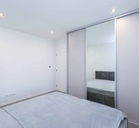 Bedroom with sliding wardrobe and bed in a family house, floor with wooden decor.