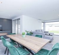 A family house with a kitchenette, a gray sofa, green chairs, and a wooden-patterned floor.