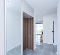 Interior of a family house with tiles, wooden panel, plant, and glass doors in the background.