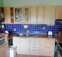 A kitchen in a family house with wooden cabinets, blue tiles, and white appliances.