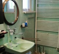 A bathroom in a family house with traditional green tiles on the wall, a mirror, and a sink.