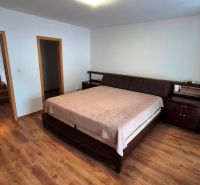 A bedroom in a three-room apartment with a bed, dark furniture, and a floor with a wood decor.