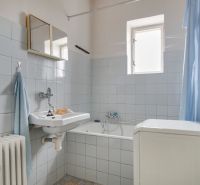 Bathroom in a family house with light tiles, a bathtub, and a washing machine.