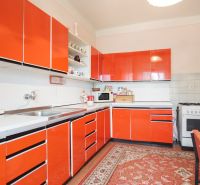 A kitchen with striking orange cabinets and a carpet in a family house.