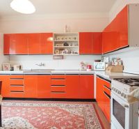 A kitchen with red cabinets and a carpet in a family house.