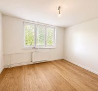 A white room in a 3-room apartment with wood-patterned flooring and a window.
