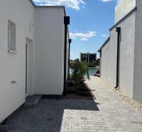 A passage between family houses in Boldog with flowers and a view of the water surface.
