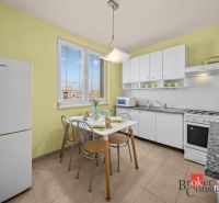 A kitchen in a 3-room apartment with a dining table, white cabinets, and appliances.