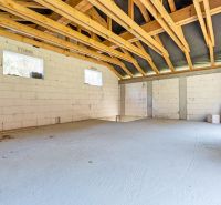 The interior of an unfinished family house with white walls and wooden beams.