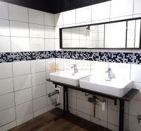 Sinks in pairs with white tiles and a wooden decor floor in commercial spaces.