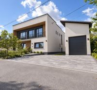 A family house in Badín with a two-story white facade and a garage surrounded by greenery.
