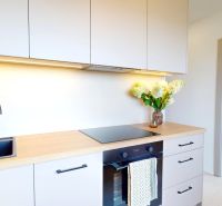A kitchen in a 3-room apartment with a cooktop, a black sink, and flowers on the counter.