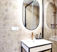 Bathroom of a 3-room apartment with stone tiles, a mirror, and a sink in a black frame.