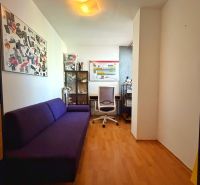 A room in a two-bedroom apartment with a purple sofa and a wooden decor floor.