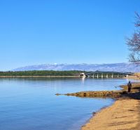 The coast in Privlaka with a view of the bridge and mountains in the background.