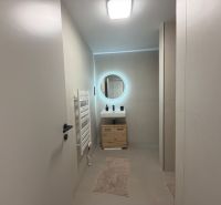 A bathroom in a 2-room apartment with a round mirror and a wooden cabinet under the sink.