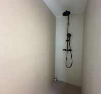 Shower corner with a black shower in a 2-room apartment, light walls, minimalist design.