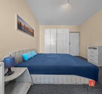 A bedroom in a 3-room apartment with a blue bed, white wardrobes, and a carpet.