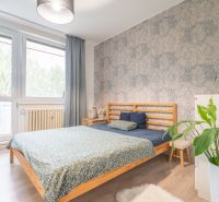 A bedroom with a double bed, a wooden decor floor, and plants in a 3-room apartment.