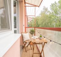 A balcony with wooden furniture and lighting in a 3-room apartment with a view of greenery.
