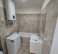 A bathroom with a bathtub, sink, and washing machine in a studio apartment, tiled with light tiles.