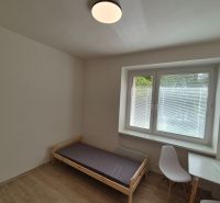 Single bed, table with a white chair, wooden decor flooring, and a window.