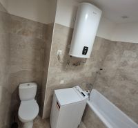 A bathroom in a studio apartment with a bathtub, washing machine, and boiler. The walls are tiled.