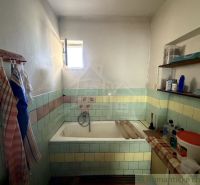 A bathroom in a family house with a bathtub, tiles, and shelves with toiletries.