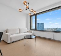 A room with a sofa, a table, a large window, and a wooden-patterned floor in a two-room apartment.