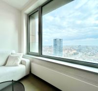 A bright living area of a 2-room apartment with a view of the city skyline through a large window.