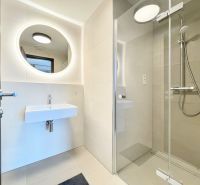 A bathroom in a 2-room apartment with a shower and a round mirror.