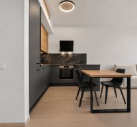 A kitchen with dark cabinets, a sofa, a dining table, and a wooden decor floor in a 2-room apartment.