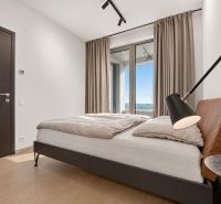 A bedroom with a double bed, a large window, and a wooden decor floor in a two-room apartment.