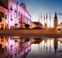 Historical buildings in Trnava are reflected in the water at dusk.