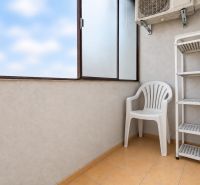 A balcony in a 3-room apartment with a plastic chair, a shelf, and air conditioning.