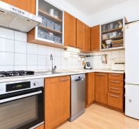 A kitchen with wooden decor, white tiles, a stove, and a stainless steel dishwasher in a three-room apartment.