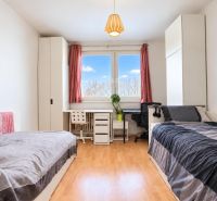 A bright room with two beds, a desk, and a floor with a wooden decor.