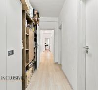 A white corridor with wooden decor, shelves, and doors leading to offices.