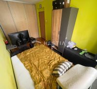 A bedroom with yellow walls, a bed, a table, and cabinets in a three-room apartment.