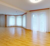 A spacious living room with a wood-patterned floor and light curtains in a family house.