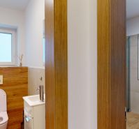 A toilet with a wooden decor wall, a sink, and a window in a family house.