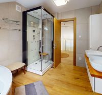 A bathroom in a family house with two sinks, a shower corner, and a floor with a wooden decor.