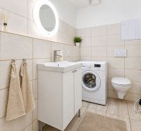 A bathroom in a studio apartment with a shower, washing machine, and ceramic tiles.