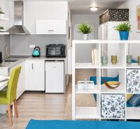 A kitchen in a one-room apartment with a dining table, a shelf, and a floor with a wooden decor.